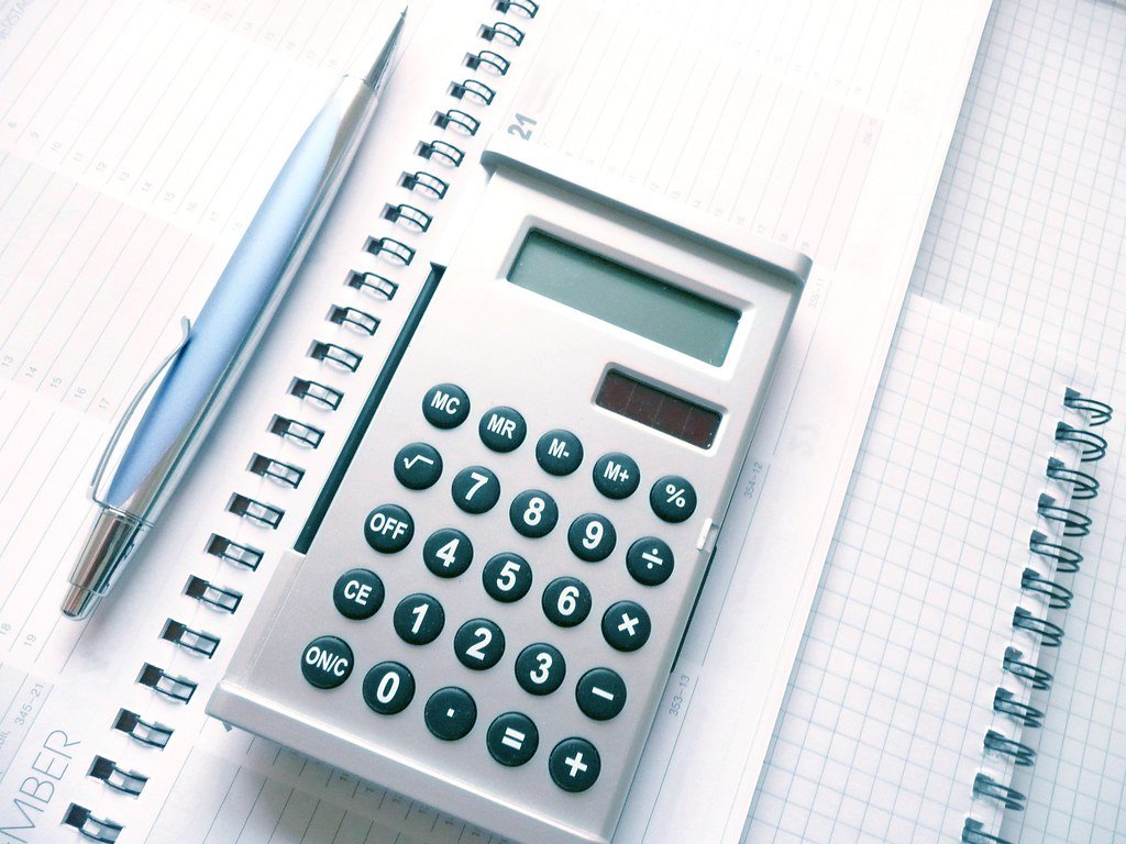 A calculator, pen and calendar on a desk